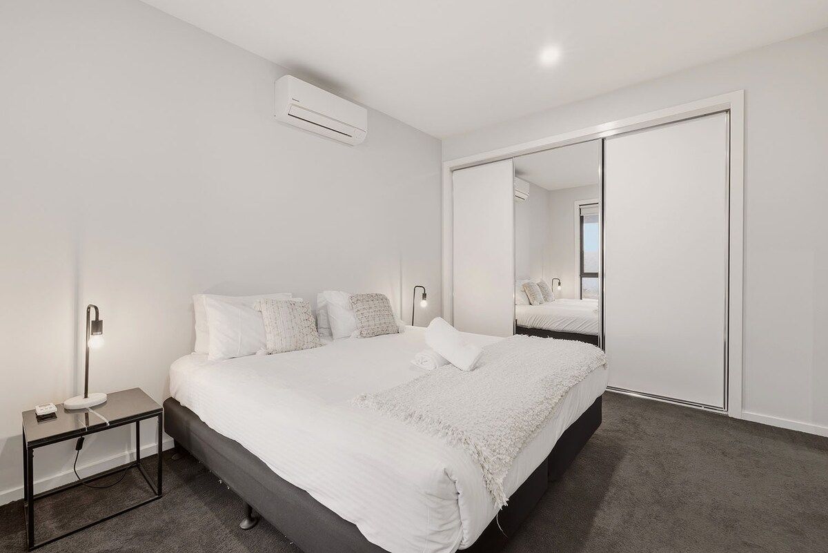 A modern bedroom with a bed, bedside table, lamp, and a large mirror.