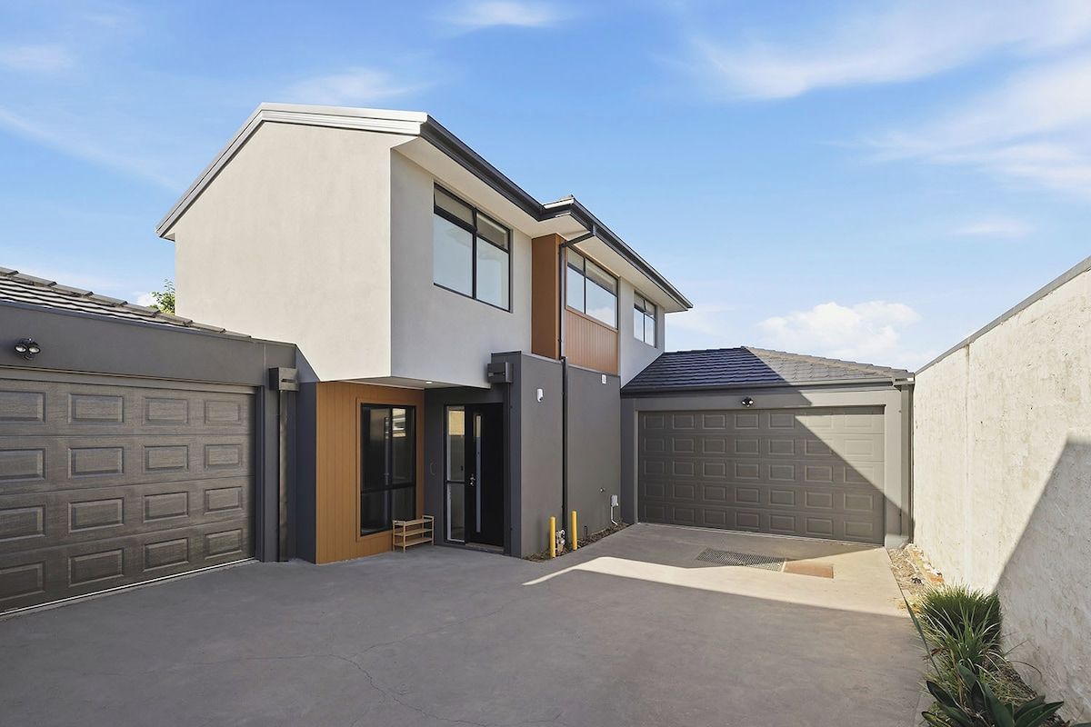 A modern two-story house with a garage, a covered entryway, and a small outdoor seating area.