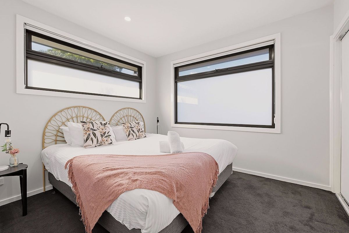 A bedroom with a bed, two bedside tables, and large windows.