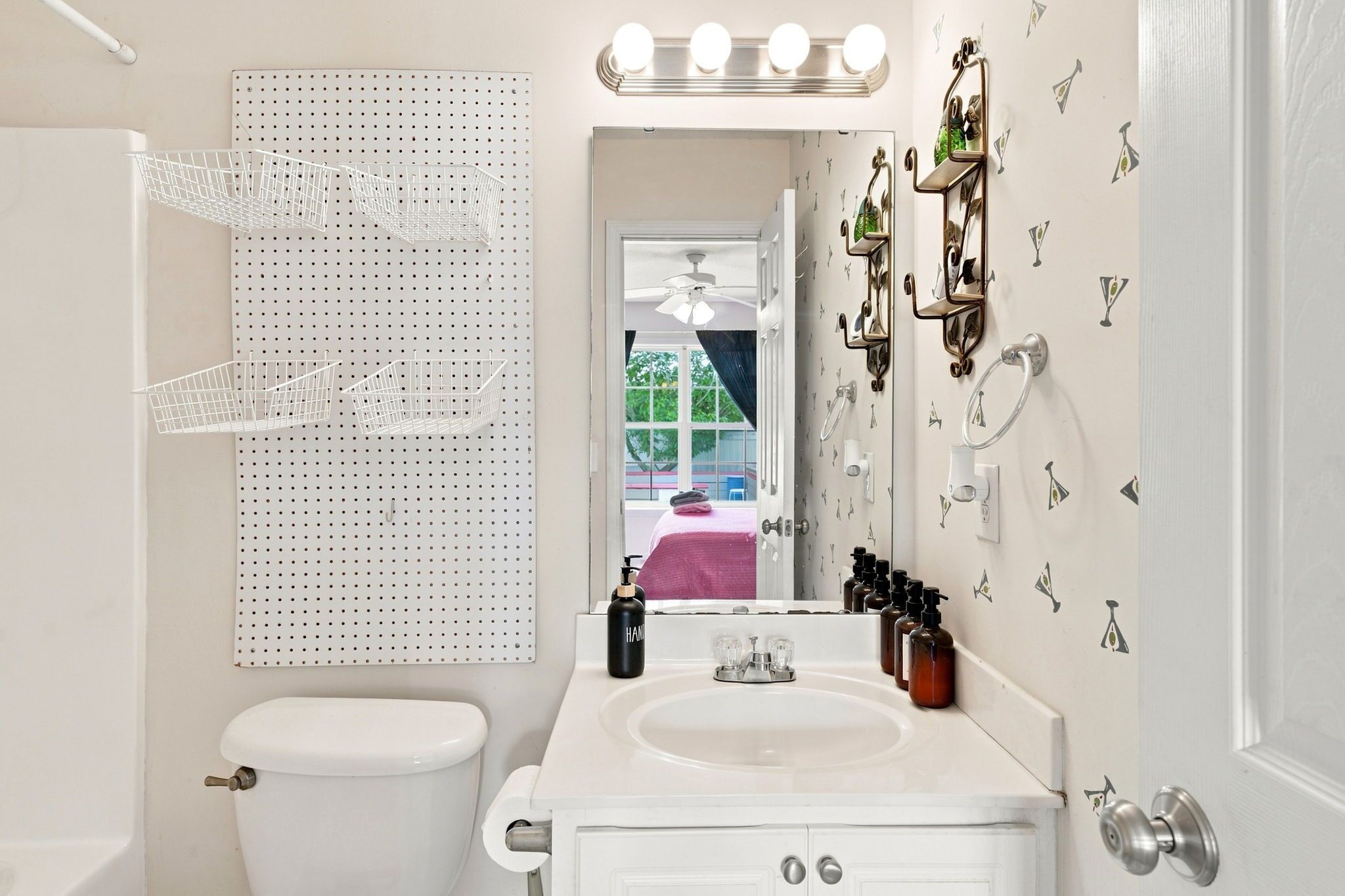 Un baño con inodoro, lavamanos, espejo con luces y un toallero de pared.