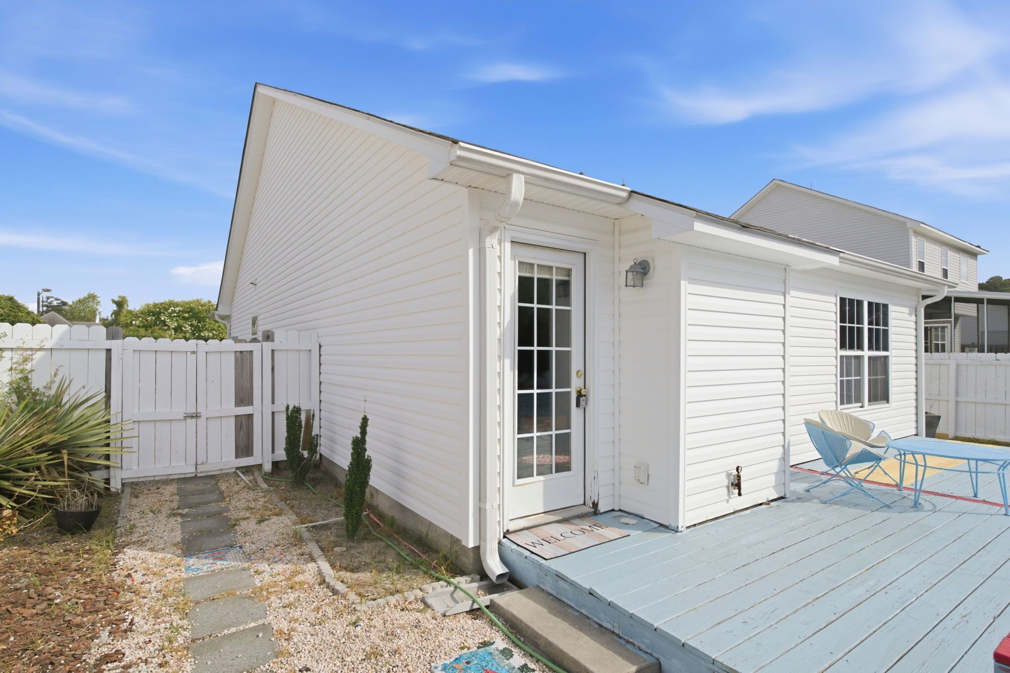 A single-story house with a front porch, a small deck, and a white picket fence.