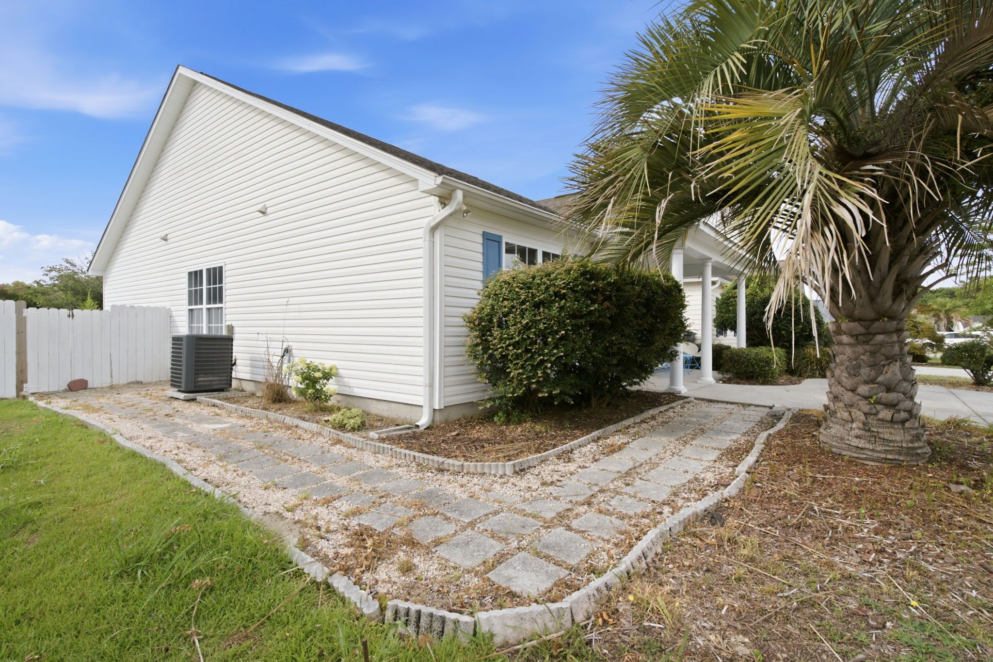 A single-story house with a paved driveway, a small lawn, and a palm tree.
