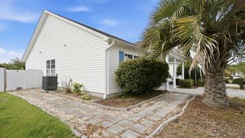 A single-story house with a paved driveway, a small lawn, and a palm tree.