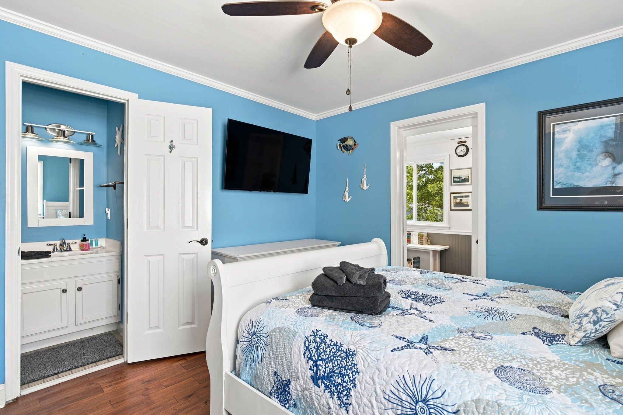 A bedroom with a bed, a television, a ceiling fan, and a door leading to a bathroom.