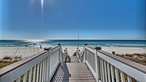 Ein hölzerner Steg führt zu einem Strand mit blauem Himmel.