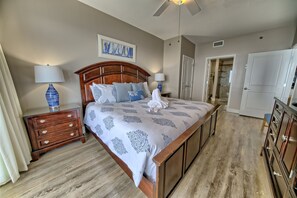 A bedroom with a large bed, wooden headboard, two bedside tables with lamps, a ceiling fan, and a door leading to a bathroom. - Sterling Breeze PCB | 3BR Luxury near Pier Park (Panama City Beach)