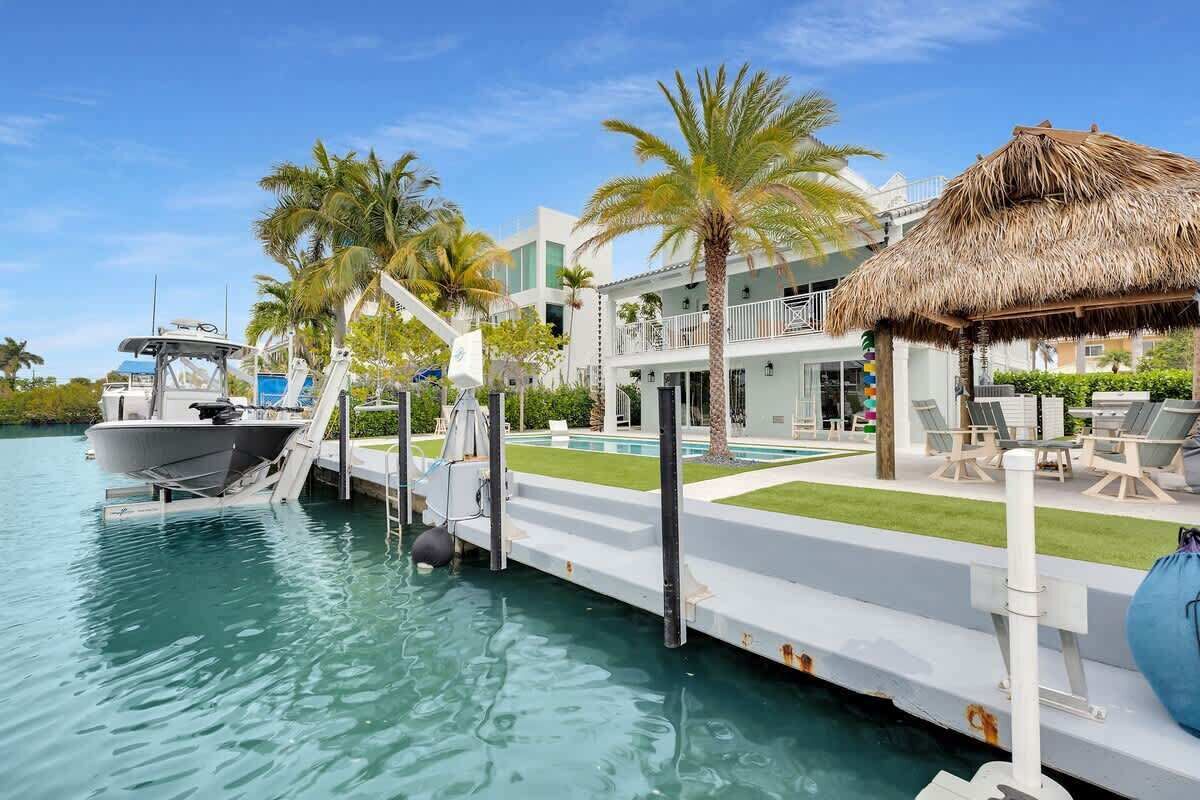 A waterfront property with a boat dock, a pool, and a thatched-roof structure.