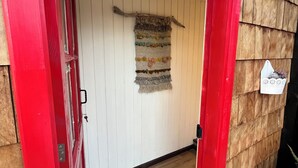 Pared exterior de madera con una puerta roja, una puerta blanca y un tapiz colgado.