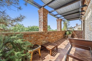 A covered patio with brick walls, wooden furniture, and potted plants. - Villa Aurelia – Luxury Istrian Stone Villa with Pool, Jacuzzi and Sauna by Istrabook (Čabrunići)