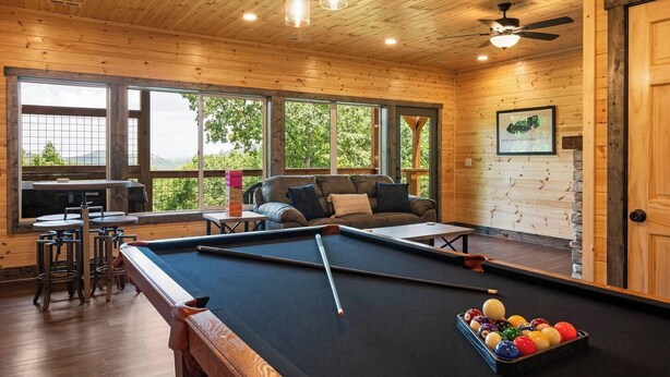 A pool table with billiard balls, a sofa, and a bar area with stools. - Nature’s Ridge | Modern Cabin + Stunning Views (Sevierville)