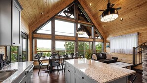 A spacious kitchen with granite countertops, a dining area with a large island, and a cozy seating area with a fireplace. - Nature’s Ridge | Modern Cabin + Stunning Views (Sevierville)