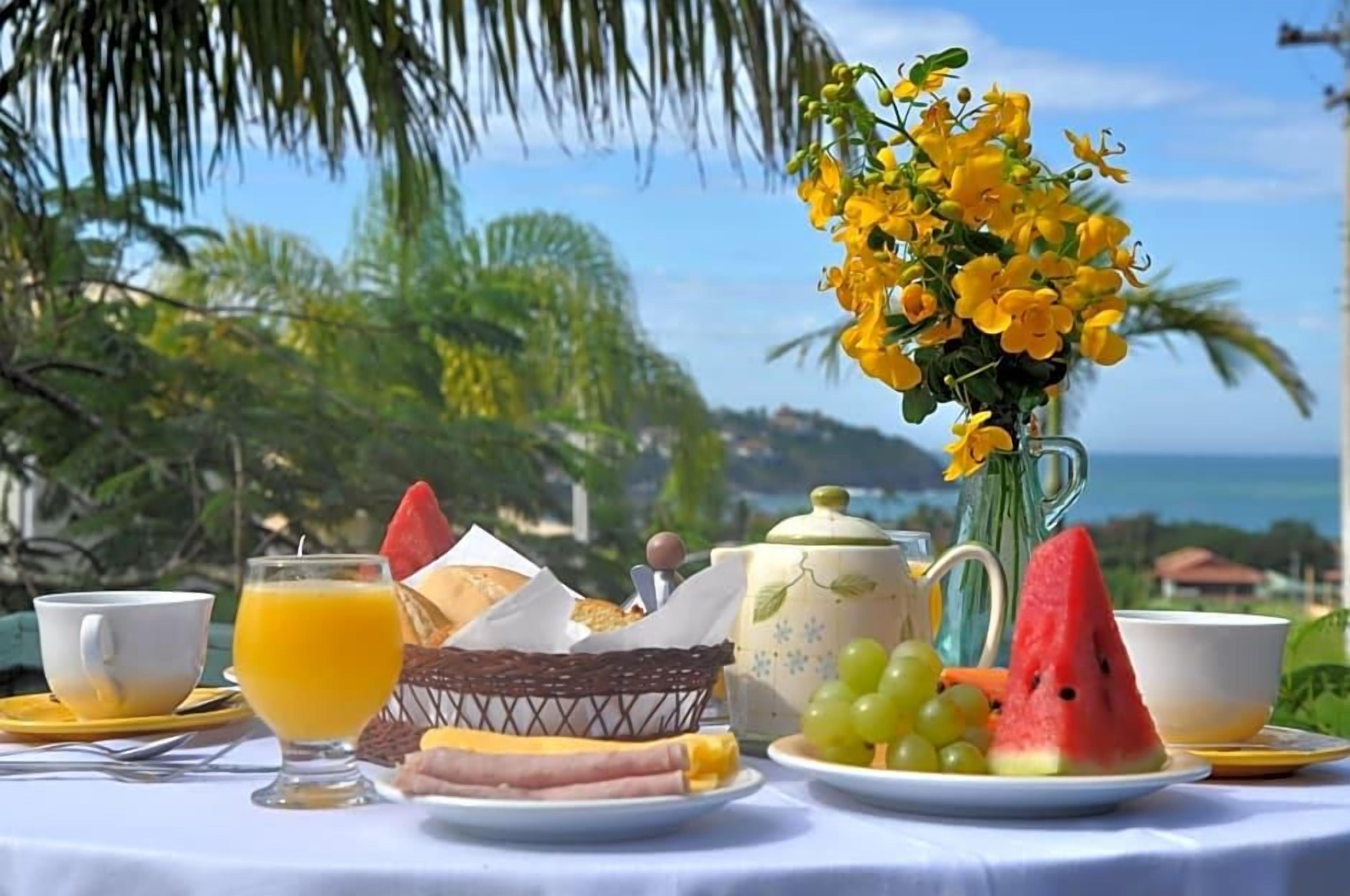 Et morgenbord med et udvalg af mad, en vase med gule blomster og udsigt til havet.