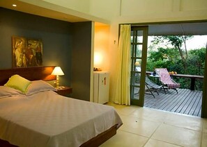 A hotel room with a bed, a nightstand, a lamp, a refrigerator, and a sliding glass door leading to an outdoor deck with a table and chairs. - Ferradura Parque Pousada (Búzios)