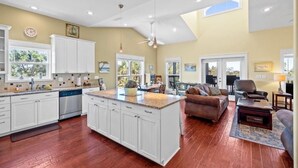 Uma sala de estar espaçosa com uma ilha grande, uma cozinha com armários brancos e uma área de jantar com vista.