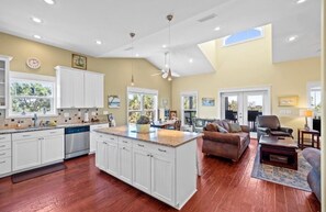 A spacious living area with a large island, a kitchen with white cabinets, and a dining area with a view. - Sunset Pointe Retreat  Bay Views • Beach Access • Pool • Kayak, Paddle Board (Port St. Joe)