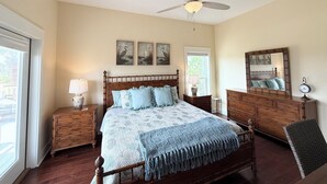 Quarto com cama, mesas de cabeceira, cômoda, ventilador de teto e quadros nas paredes.