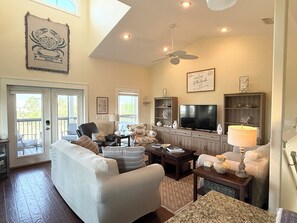 A living room with a sofa, armchairs, a television, and a ceiling fan. - Sunset Pointe Retreat  Bay Views • Beach Access • Pool • Kayak, Paddle Board (Port St. Joe)