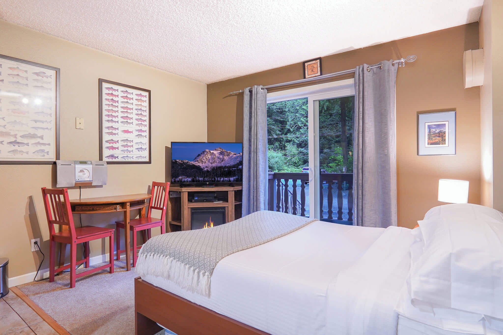 A hotel room with a bed, a desk with a chair, a television, and a window with a view of trees.