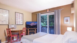 A hotel room with a bed, a desk with a chair, a television, and a window with a view of trees. - Fireside Suite, Simple Basecamp at Snowline Lodge (Deming)