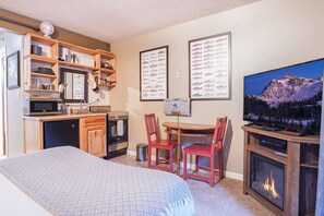 A compact hotel room with a kitchenette, a dining area, a bed, and a fireplace.