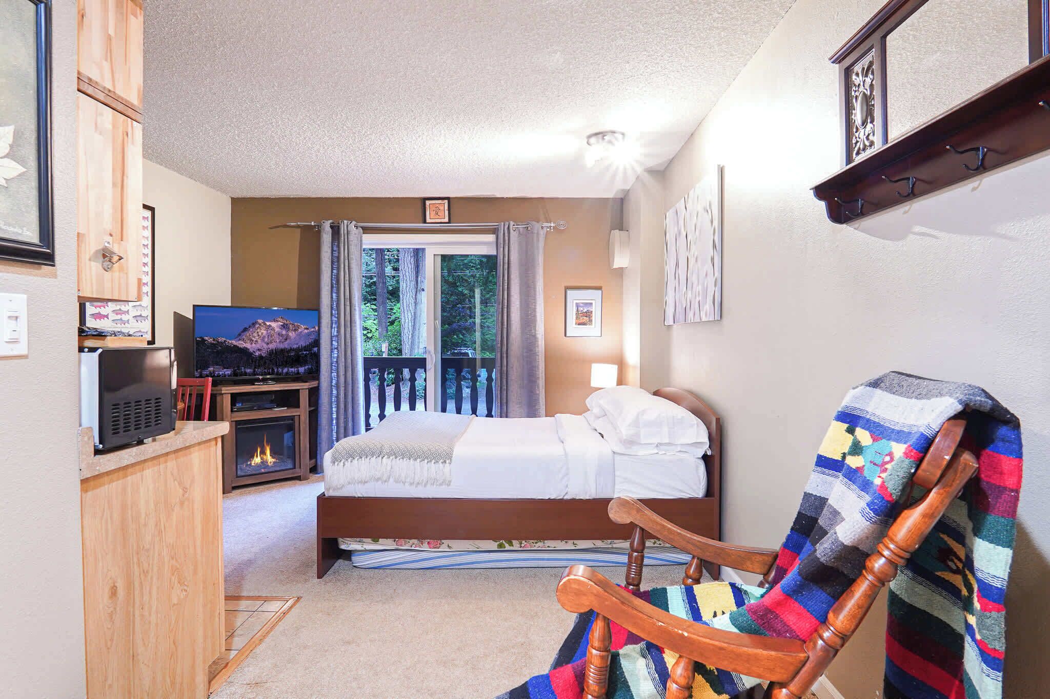 Un dormitorio con cama, televisor, chimenea y balcón con vistas a árboles.