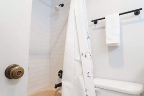 Une salle de bain avec des toilettes blanches, un rideau de douche et un porte-serviettes.