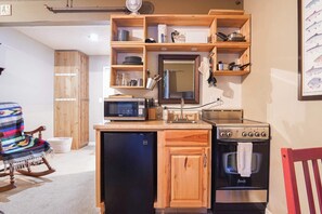 A compact kitchen with wooden cabinetry, a microwave, a stove, and a refrigerator.