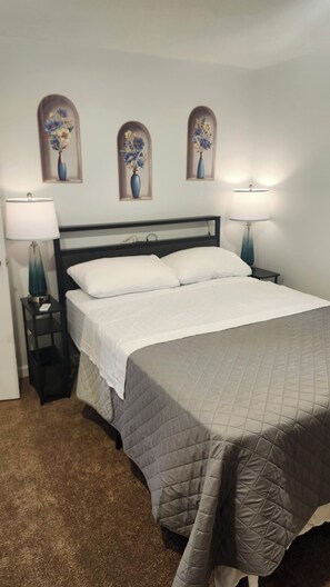A bedroom with a bed, two bedside tables, lamps, and three wall-mounted flower paintings. - Creekside Caper (Mount Hope)