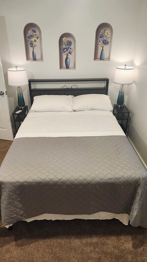 A neatly made bed with a quilted cover, two bedside lamps, and three wall-mounted vases with floral designs. - Creekside Caper (Mount Hope)