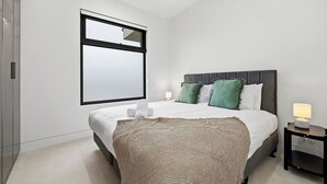 Moderni hotellihuone, jossa on suuri sänky, ikkuna ja yöpöytä, jossa on lamppu.