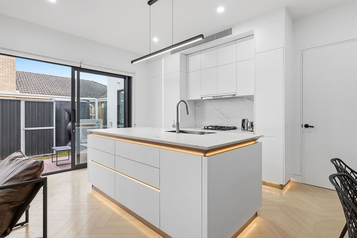 A modern kitchen with a central island, white cabinetry, and a sliding glass door leading to an outdoor area.