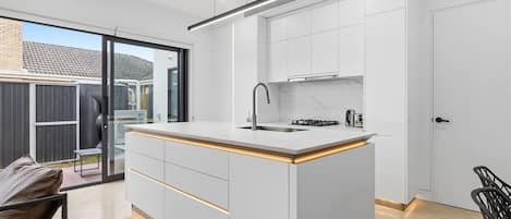 A modern kitchen with a central island, white cabinetry, and a sliding glass door leading to an outdoor area.