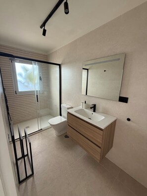 Un bagno moderno con doccia, servizi igienici e lavandino, dotato di un ampio specchio e porta scorrevole in vetro.