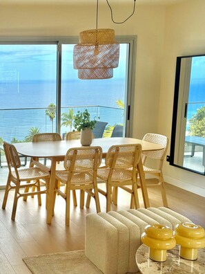 A dining area with a round table, six wicker chairs, a woven pendant light, and a view of the ocean through large windows. - White House • Relaxation, Views, and an Infinity Pool • (Santa Úrsula)