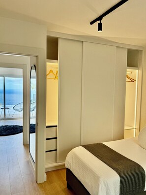 Ein Schlafzimmer mit einem Bett, einem Kleiderschrank und Meerblick durch eine Glastür.