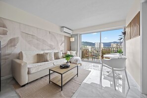 Ein modernes Wohnzimmer mit einer Couch, einem Couchtisch und einem Balkon mit Blick auf Gebäude und Berge.