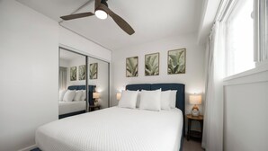 A bedroom with a bed, a ceiling fan, a nightstand with a lamp, and a window with curtains. - Free Parking & Beach Gear at 2BR Iconic Whale Building Condo (Honolulu)