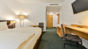 Una habitación de hotel con una cama, un escritorio, una silla, un televisor y una puerta.
