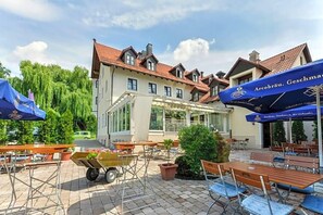 An outdoor seating area with tables and chairs, a covered section, and a building with a tiled roof. - Nagerl Landhotel (Marzling)
