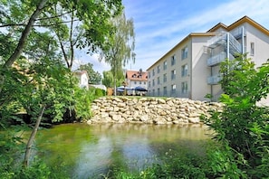 A building with a stone retaining wall, a small pond, and lush greenery. - Nagerl Landhotel (Marzling)