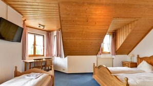 Una habitación con dos camas de madera, televisión y ventana con cortinas.
