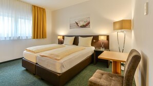 Habitación de hotel con cama doble, escritorio, silla, lámpara y un cuadro en la pared.