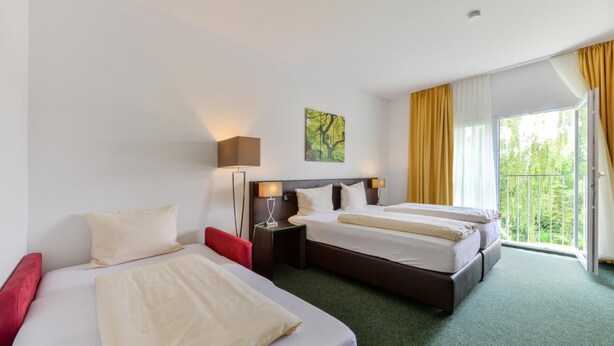 Habitación de hotel con dos camas, una silla roja, un cuadro en la pared y un balcón con cortinas amarillas.