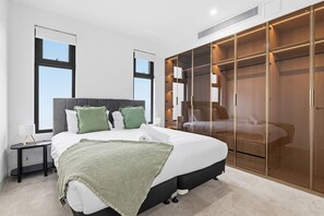 A bedroom with a large bed, a walk-in closet, and a window. - Domi Rentals - The Cheltenham Southland House (Cheltenham)