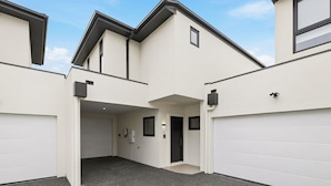 A modern building with a covered parking area, a garage door, and a small window. - Domi Rentals - The Cheltenham Southland House (Cheltenham)