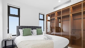 A bedroom with a large bed, a bedside table, a wardrobe, and a window. - Domi Rentals - The Cheltenham Southland House (Cheltenham)