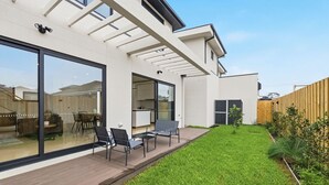 Een modern huis met een terras, een glazen deur die leidt naar een eethoek, en een houten omheining.
