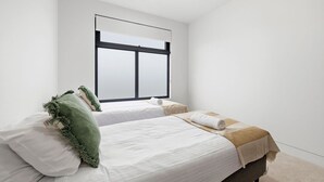 Een slaapkamer met twee bedden, een groot raam en een effen witte muur.