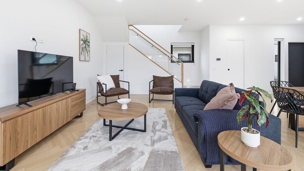 Een moderne woonkamer met een flatscreen televisie, houten meubels, een blauwe bank en een trap naar een andere kamer.