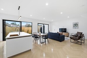 Un espace de vie moderne comprenant un îlot de cuisine, un coin repas, un canapé, une télévision et une vue sur l’extérieur.